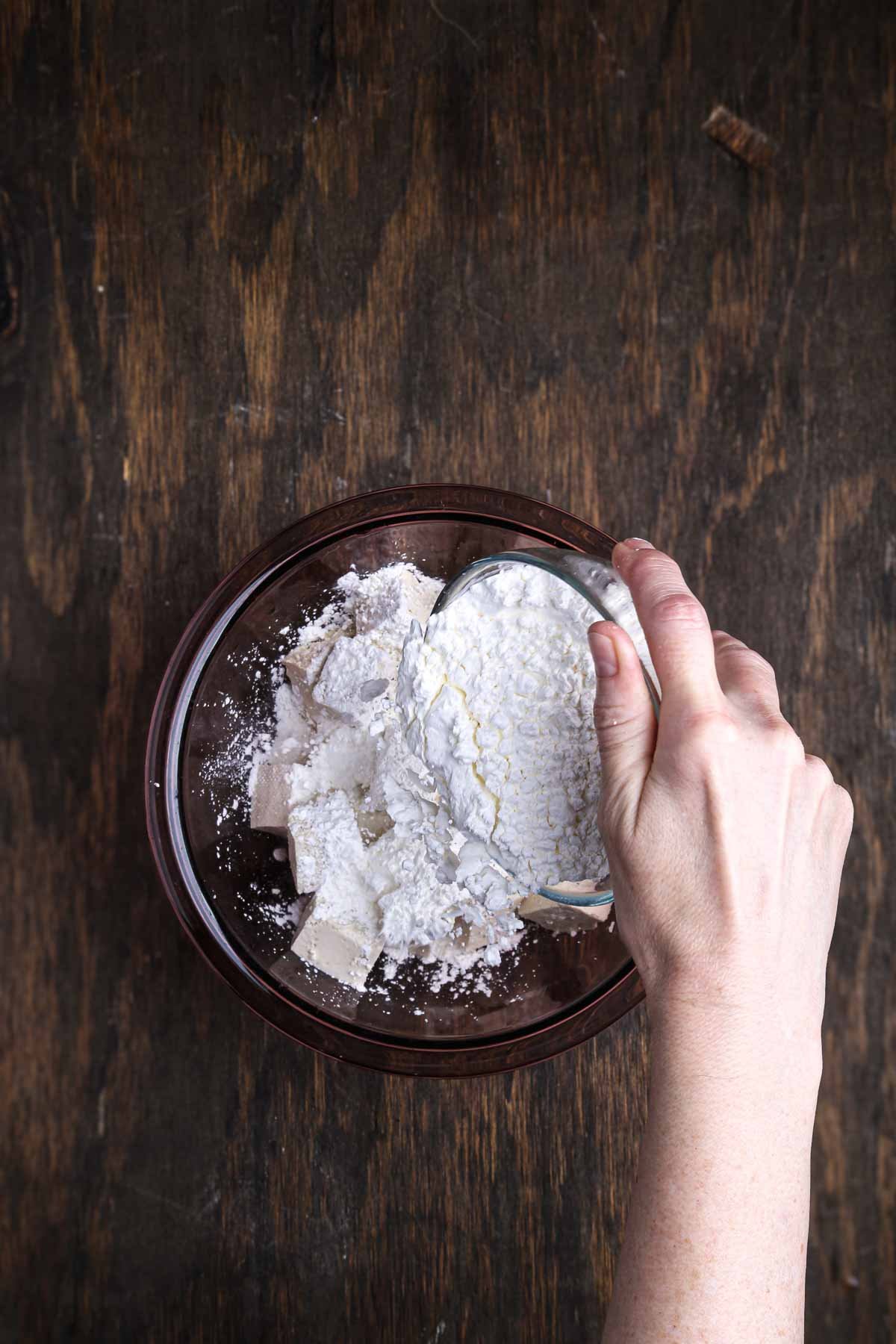 Cornstarch being poured over tofu cubes to create a crisp coating.
