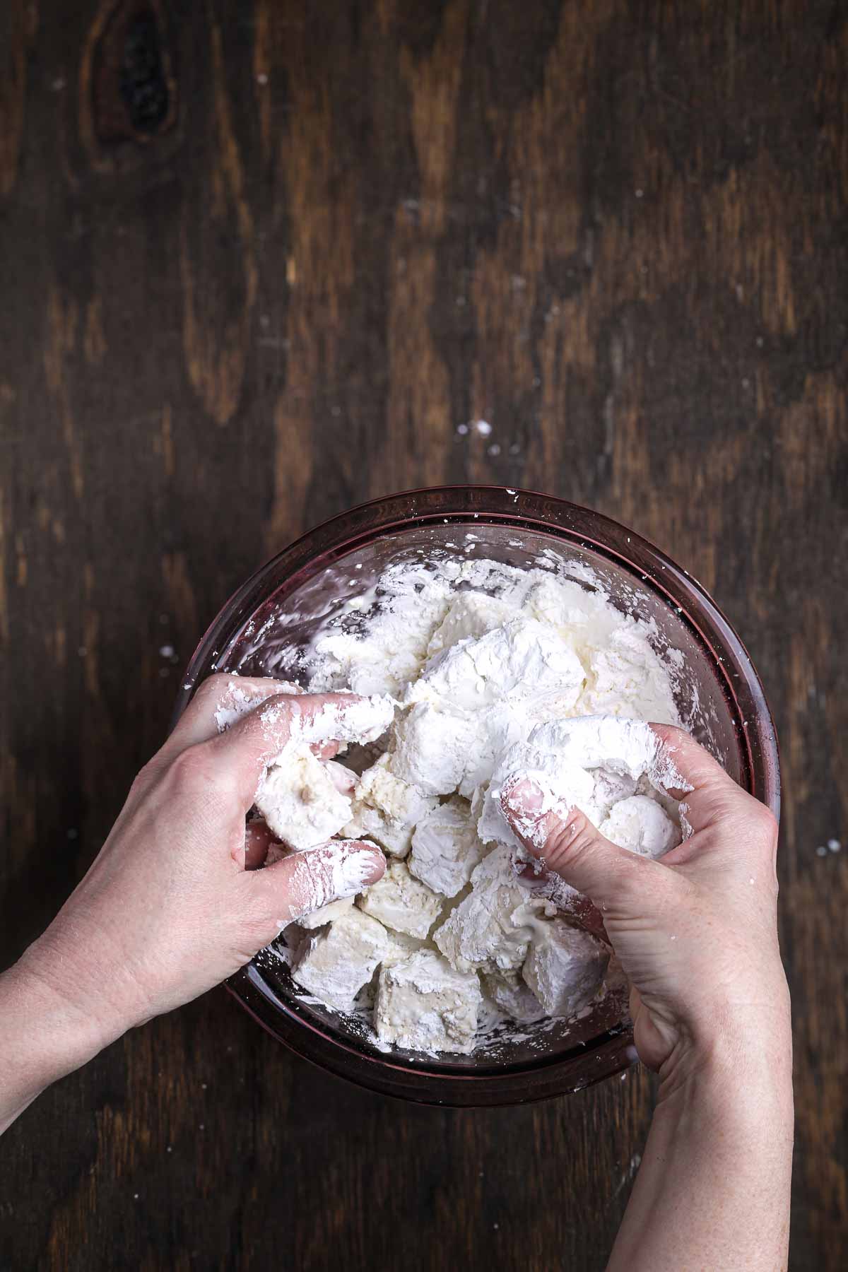 Hands coating tofu cubes evenly with cornstarch mixture.