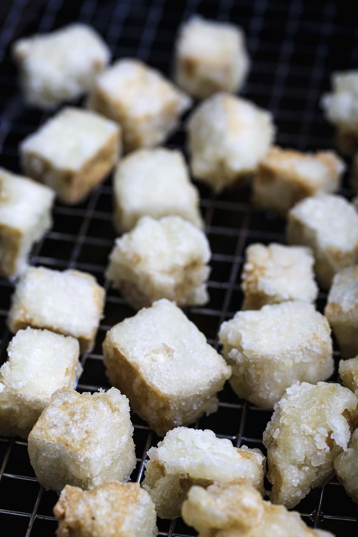 Crispy golden tofu cubes resting on a wire rack after frying.