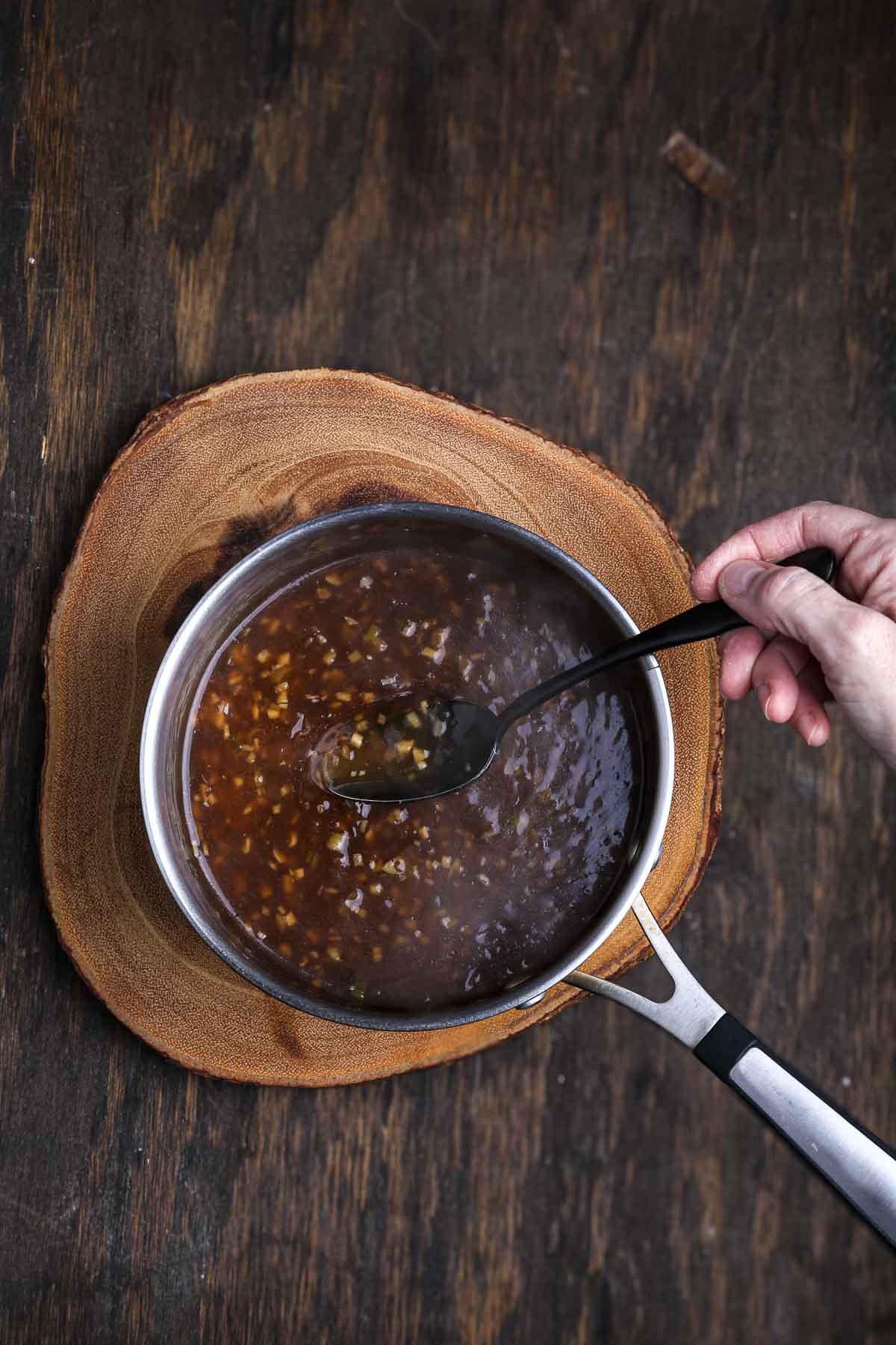 Sweet and savory sauce thickening in a saucepan, stirred with a spoon.