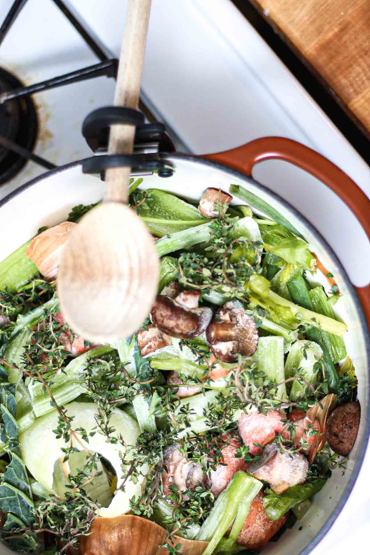 Fresh and frozen vegetables with thyme in a Dutch oven before making vegan stock.