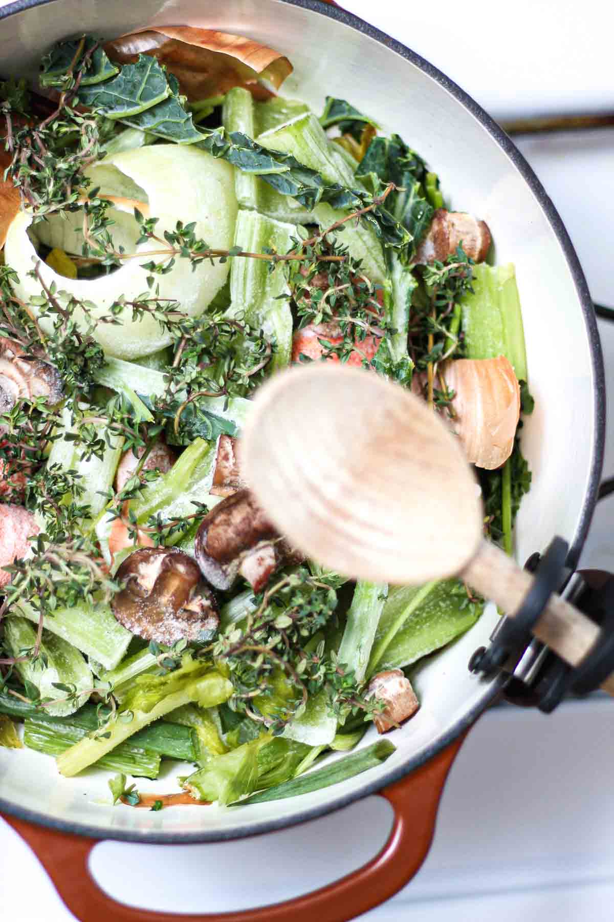 Top view of vegetable scraps, mushrooms, celery, and herbs for vegan stock preparation.
