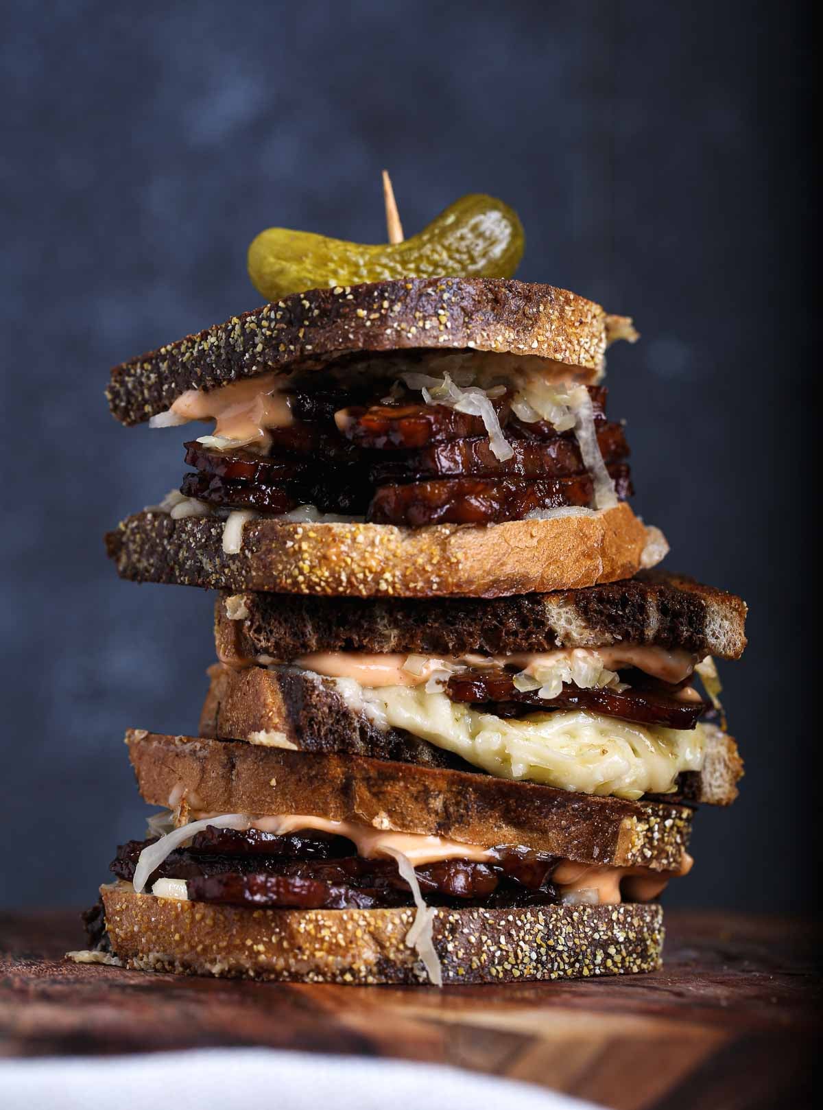 A stack of vegan tempeh Reuben sandwiches on rye bread with sauerkraut, vegan cheese, and sriracha mayo, showing tempeh as a high-protein plant-based protein source.