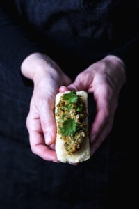 Hands holding a piece of crispy fried tofu filled with savory lemongrass-peanut sauce and garnished with cilantro.
