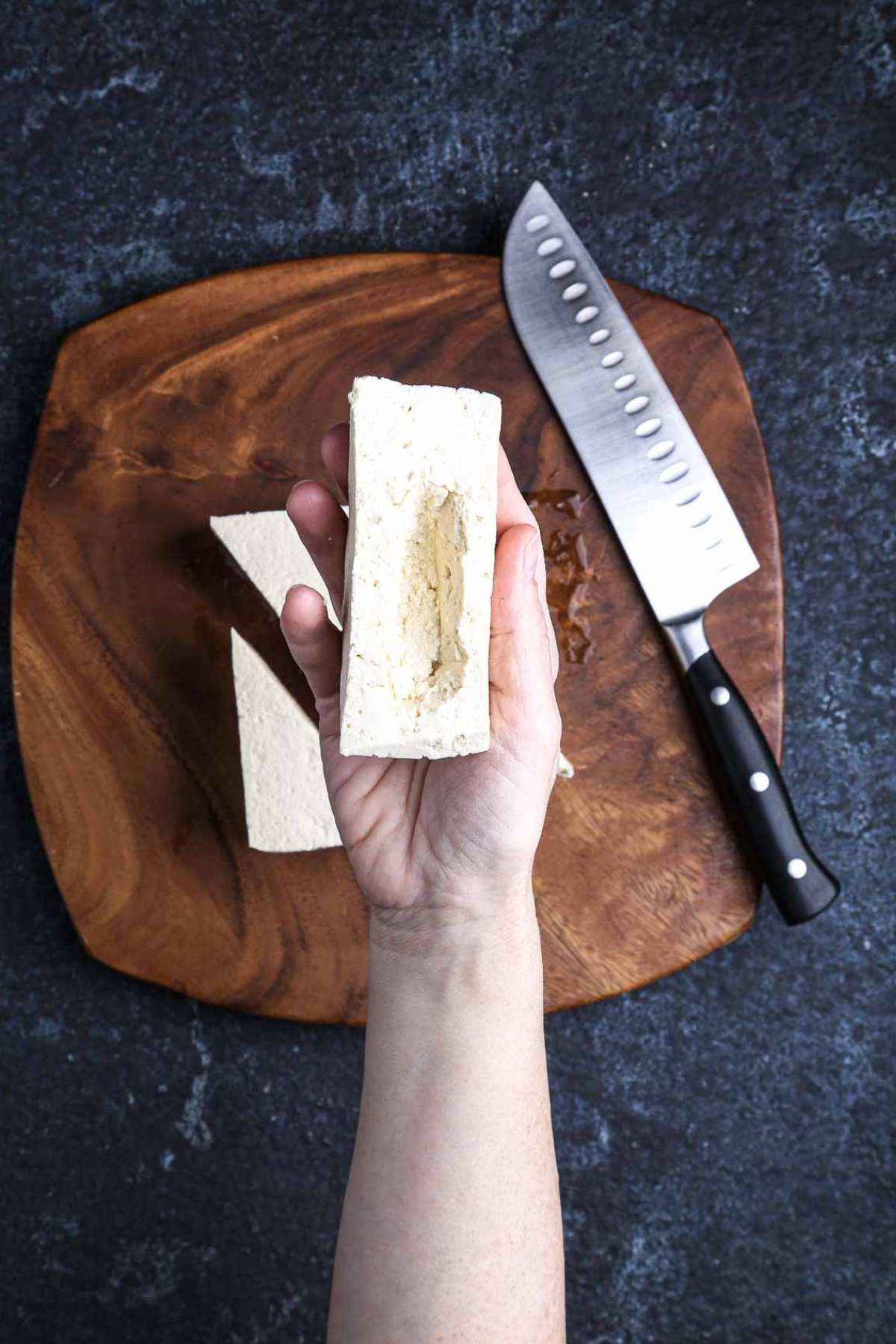 Hand holding a triangle of firm tofu with a hollowed-out center, ready to be filled with lemongrass-peanut sauce.