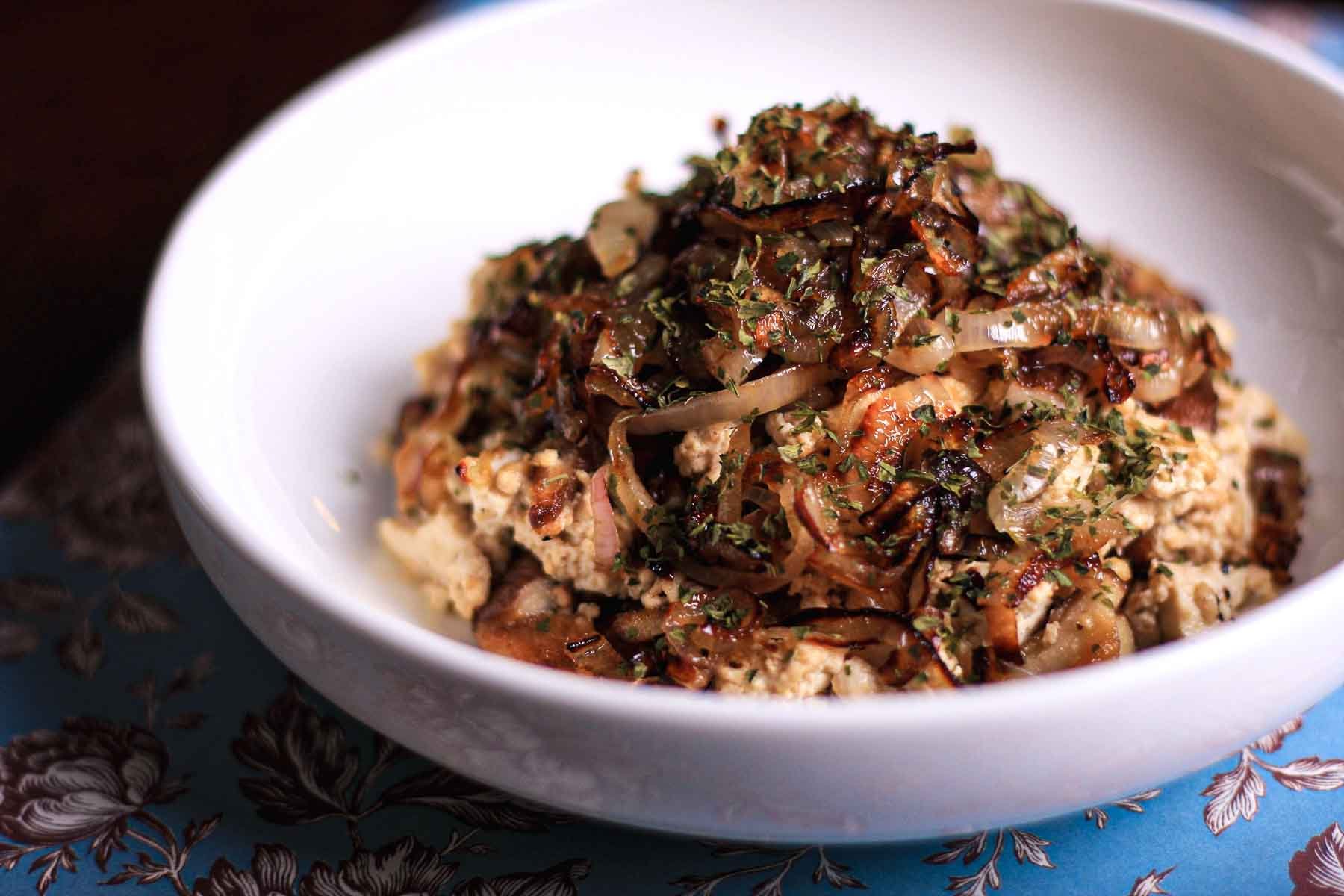 Close-up of tofu scramble with seared shiitakes and golden caramelized shallots in a white bowl.