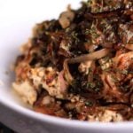Close-up of tofu scramble topped with caramelized shallots and shiitake mushrooms in a white bowl.