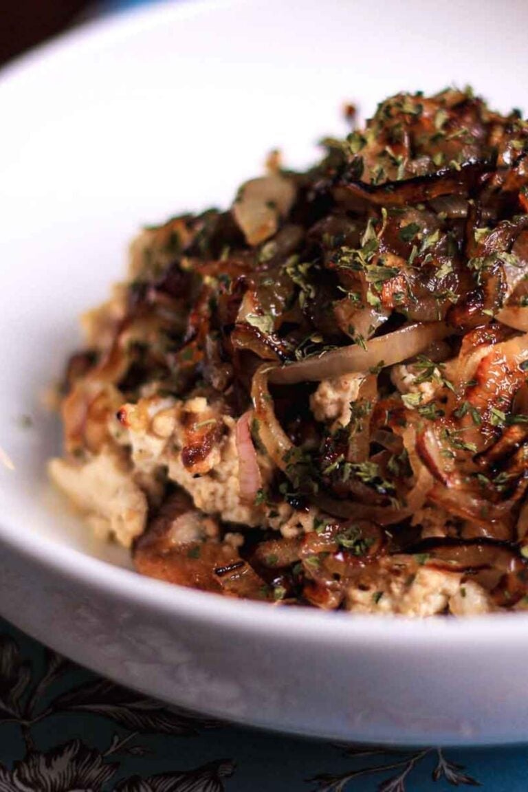 Close-up of tofu scramble topped with caramelized shallots and shiitake mushrooms in a white bowl.