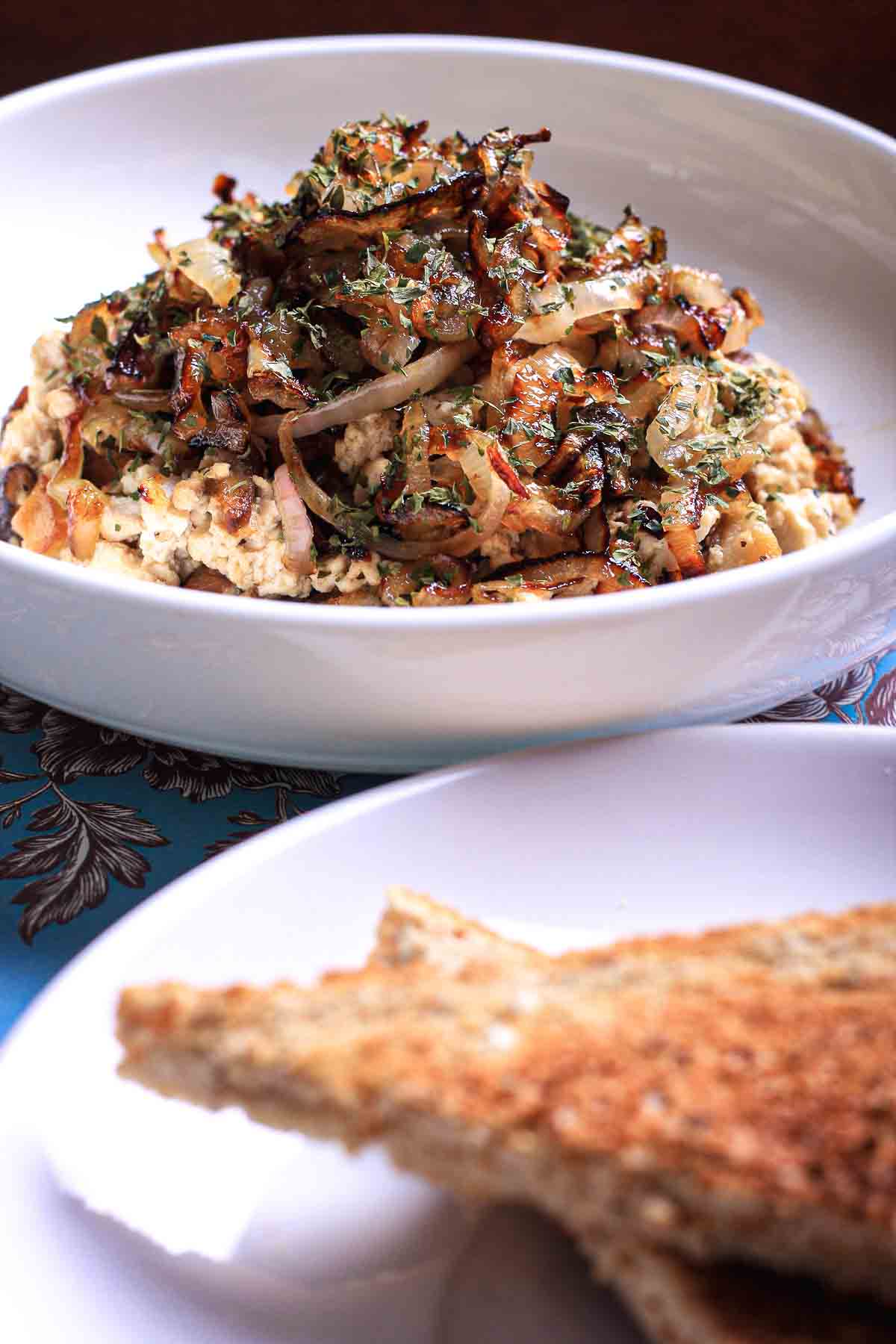 Bowl of tofu scramble layered with caramelized shallots and browned shiitake mushrooms, served with toast.