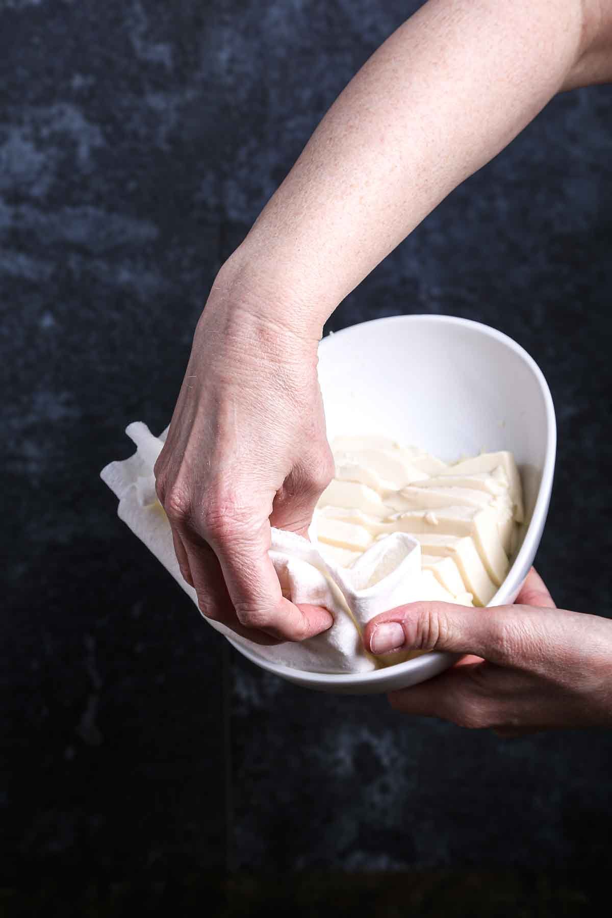 Gently draining excess moisture from silken tofu after steaming.