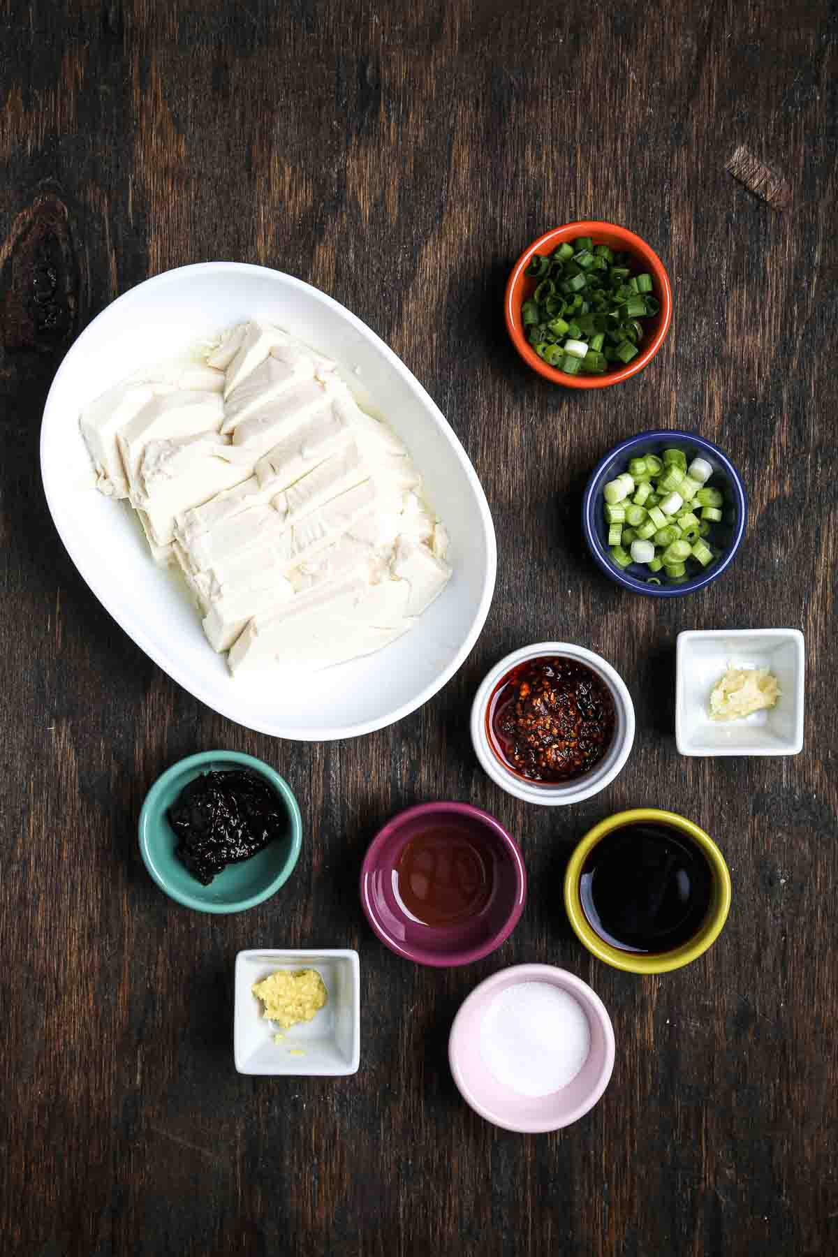 Ingredients for steamed tofu with fermented black bean sauce, including silken tofu, scallions, ginger, garlic, chili crisp, sesame oil, and tamari.