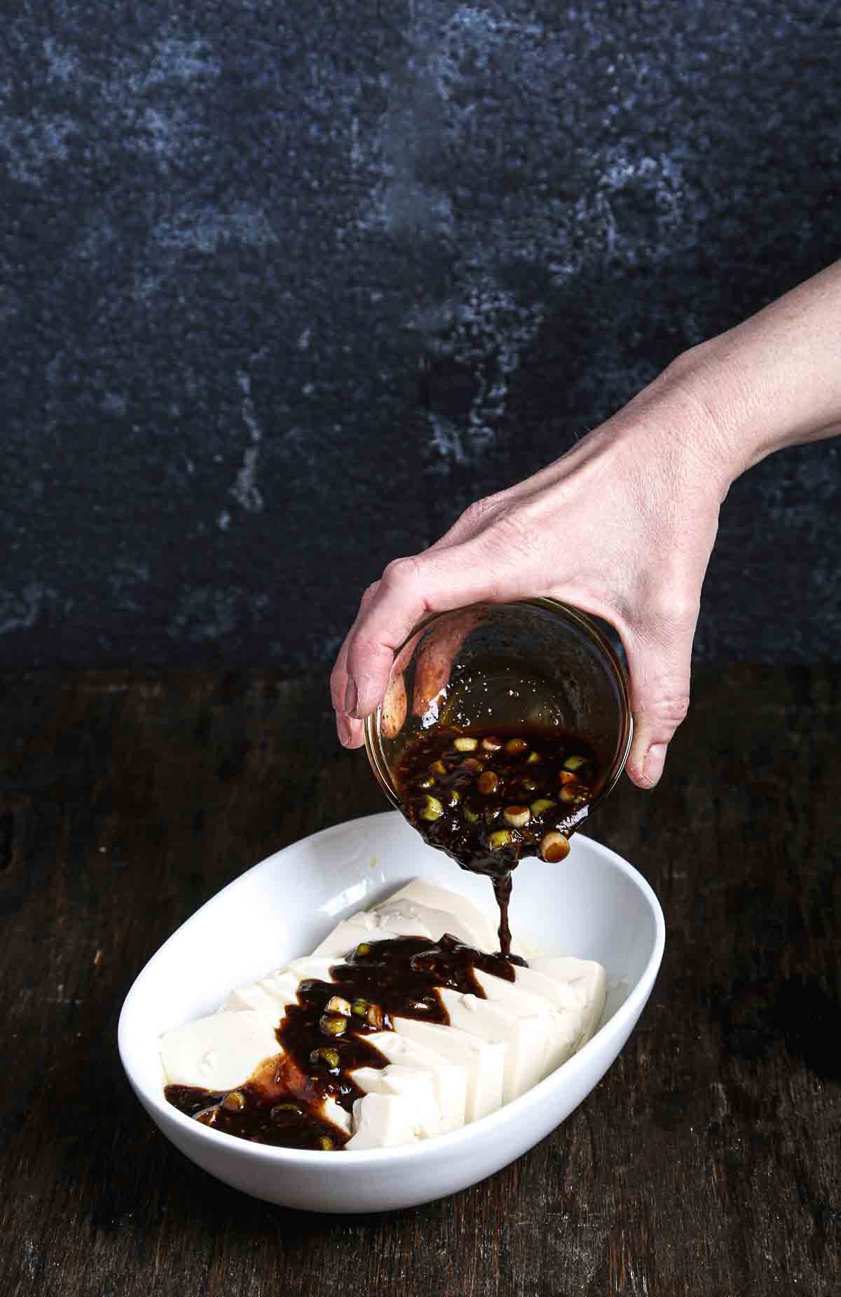 Pouring fermented black bean sauce over warm steamed tofu before serving.