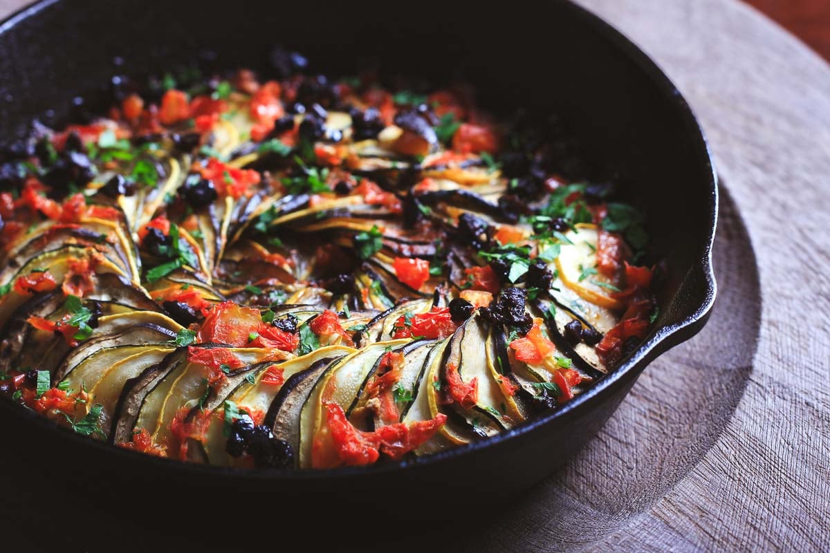 Side angle of layered ratatouille in cast iron skillet with slow-roasted summer vegetables.