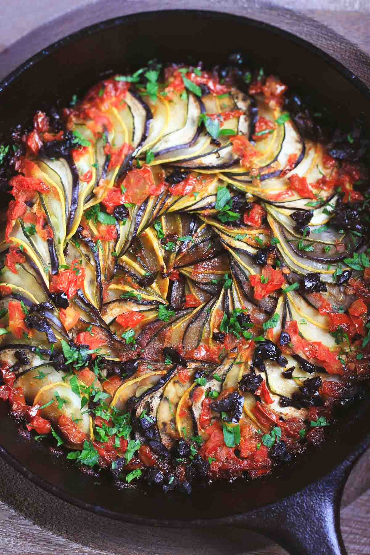 Close-up of roasted ratatouille with caramelized edges, chopped olives, and fresh parsley garnish.