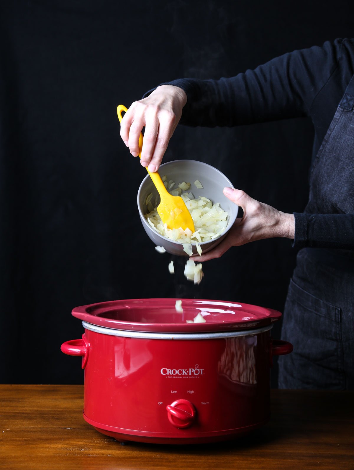 Sautéed onions being added to the slow cooker as part of the stuffing layers.