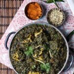 Overhead view of vegan palak paneer served in a metal bowl, surrounded by fennel seeds, curry powder, and green chiles.