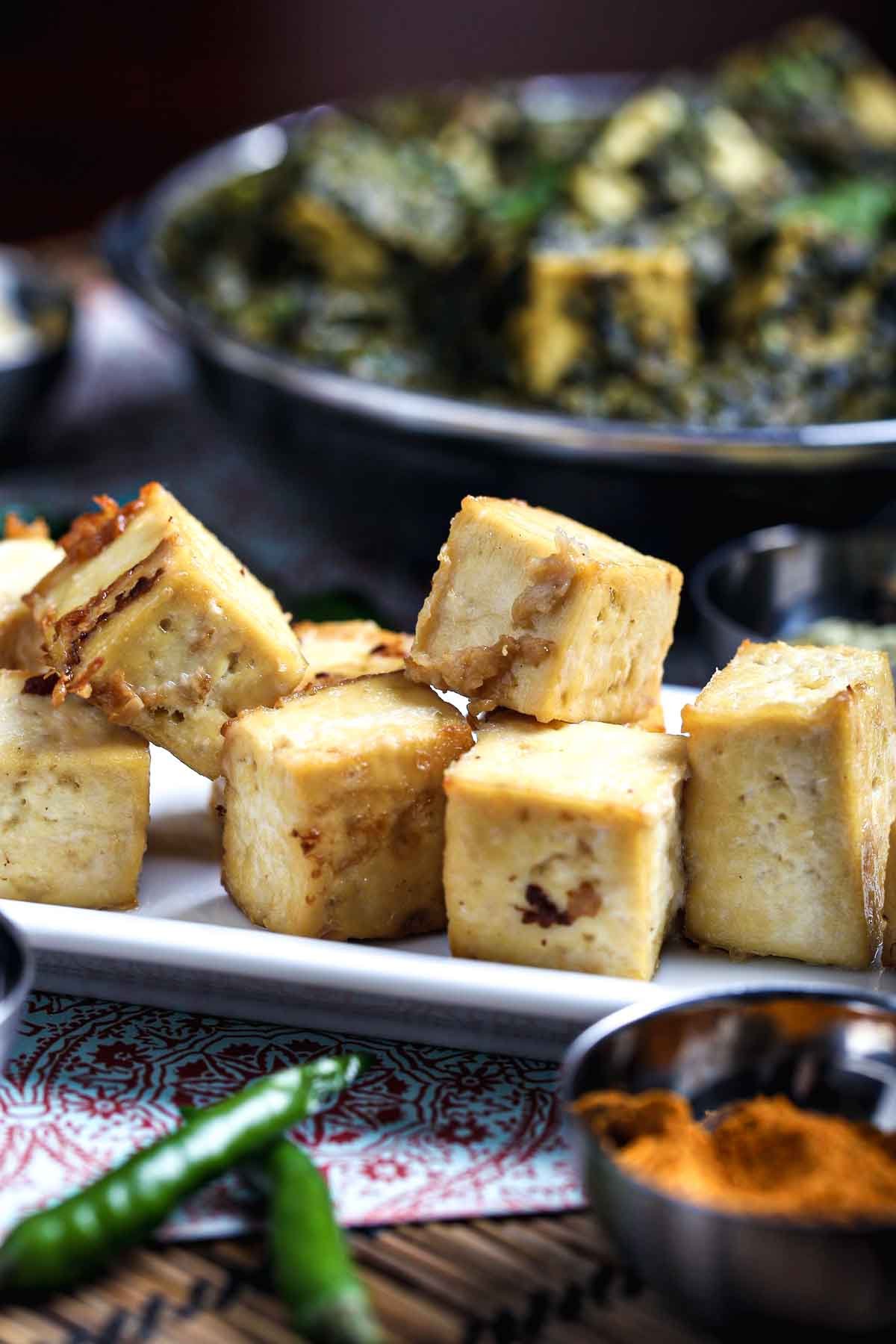 Baked tofu paneer cubes on a white plate with lightly browned edges, ready to be added to vegan palak paneer.
