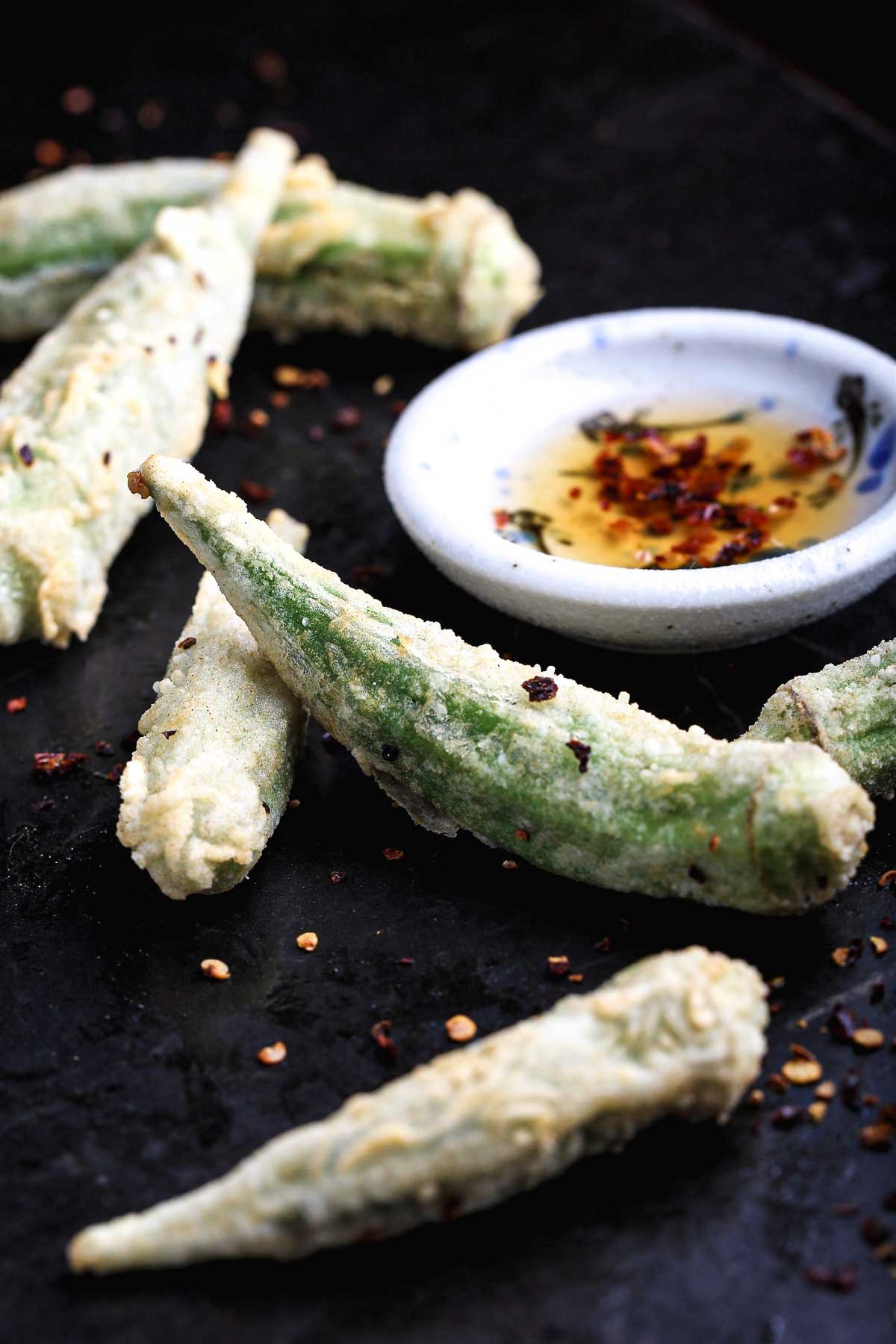 Whole fried okra pods arranged with vinegar dipping sauce and chili flakes.