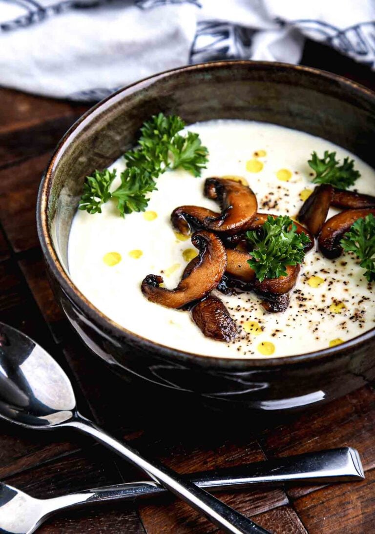 Bowl of cauliflower soup served with mushrooms and parsley on a wooden table.