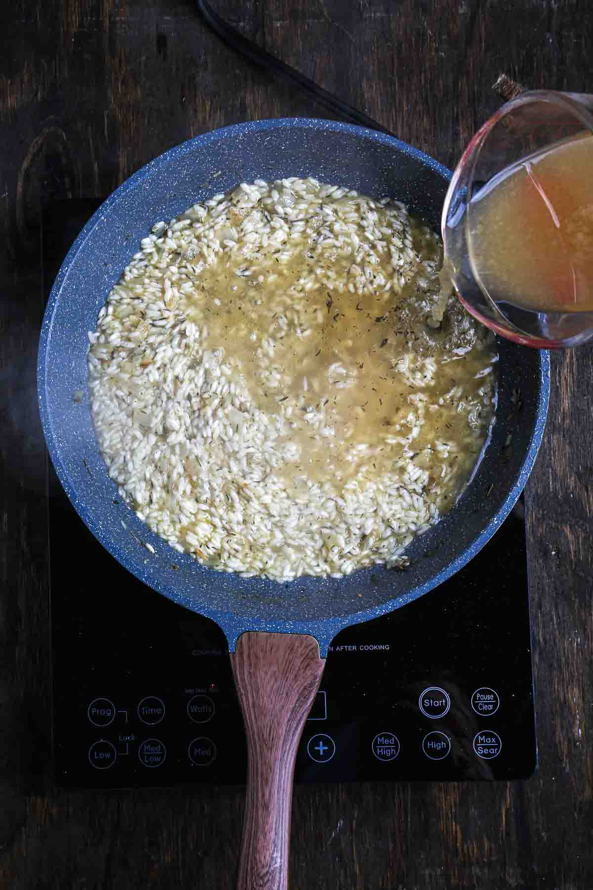 Warm vegetable stock poured into arborio rice during risotto cooking.
