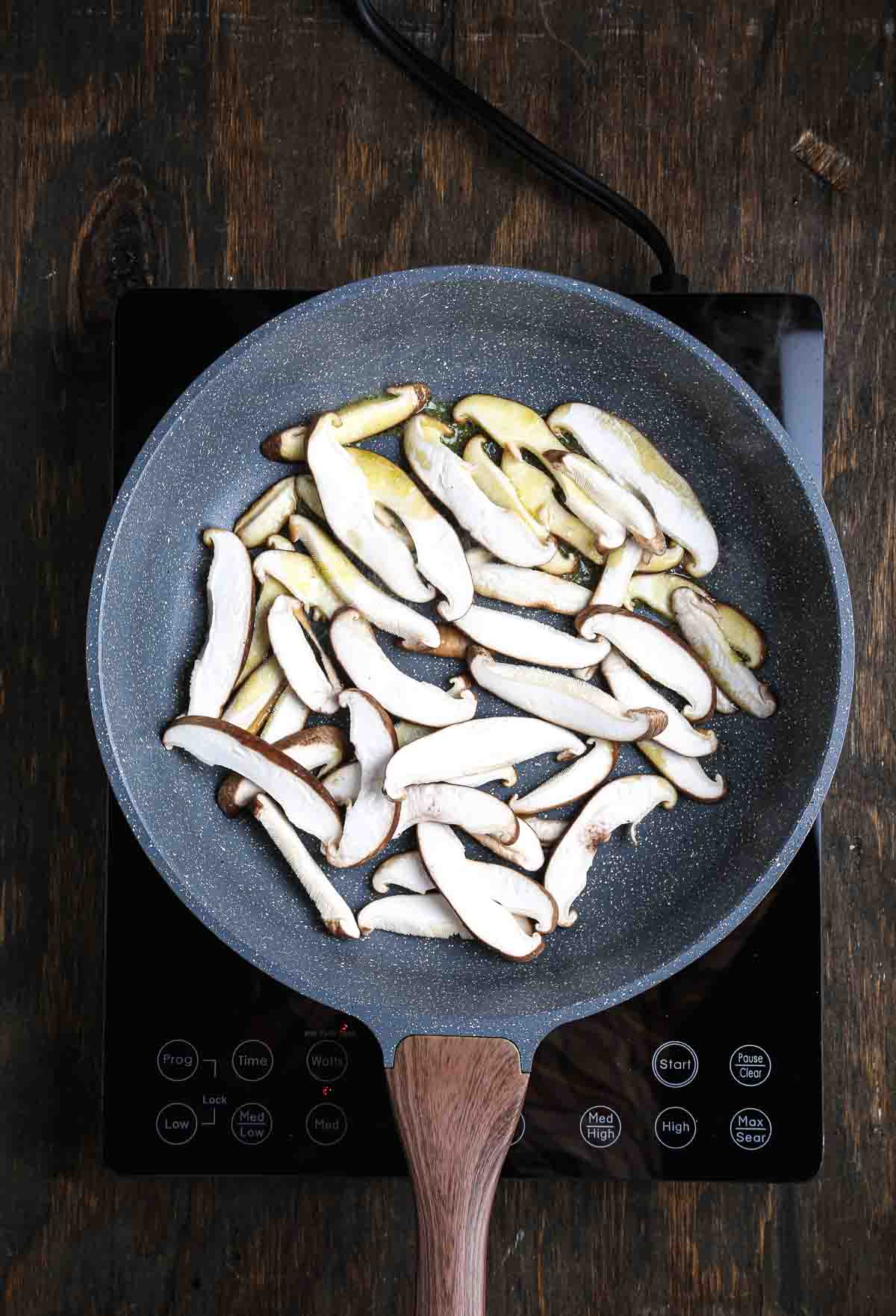 Sliced shiitake mushrooms starting to sear in a pan for vegan mushroom risotto.