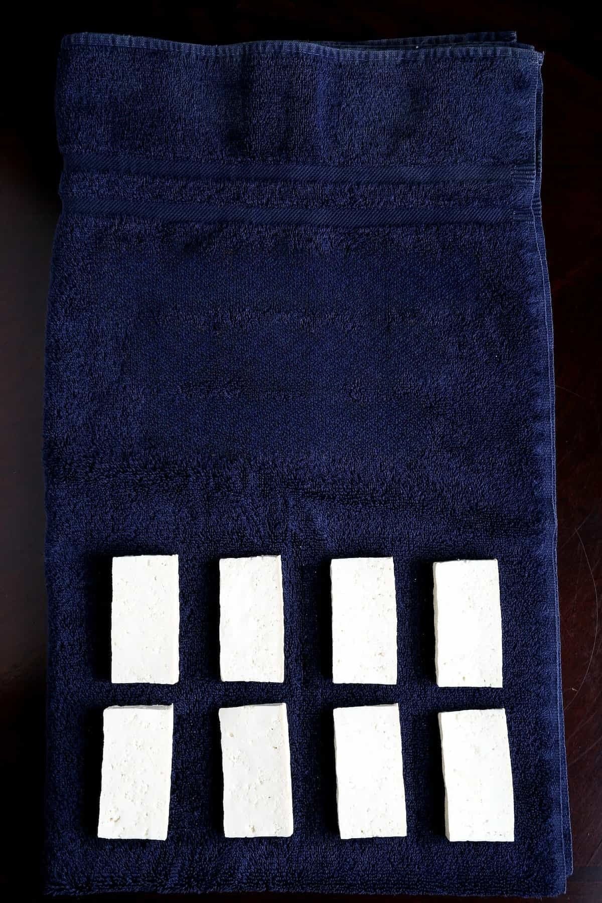 Eight tofu slabs laid out evenly on a thick bath towel before pressing.