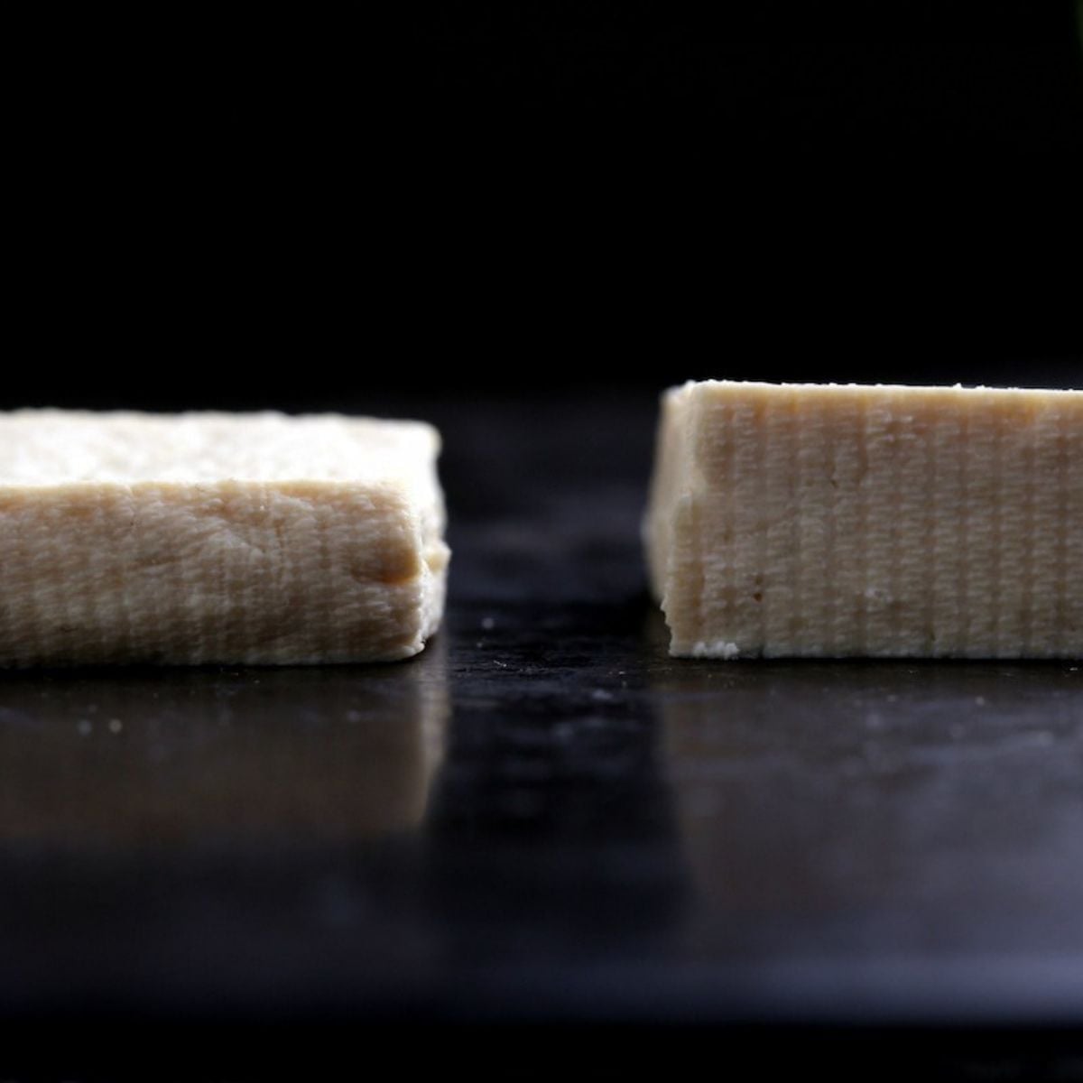 Two pressed tofu slabs side by side showing texture difference between towel method and paper towel method.