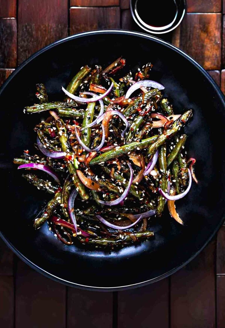 Spicy grilled green beans tossed with sambal, sesame seeds, and red onion, served in a black bowl.