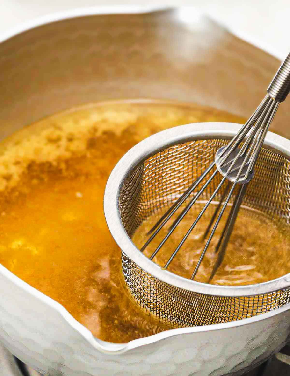 Dissolving miso paste into hot vegan dashi broth using a fine mesh strainer.