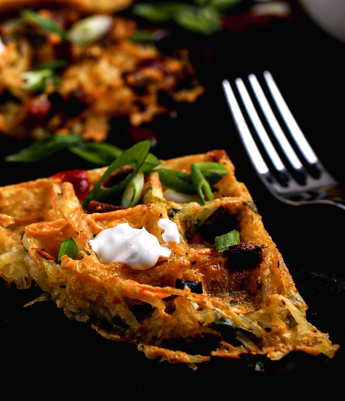 Angled view of savory hash brown waffle slice topped with scallions and a dollop of dairy-free sour cream.