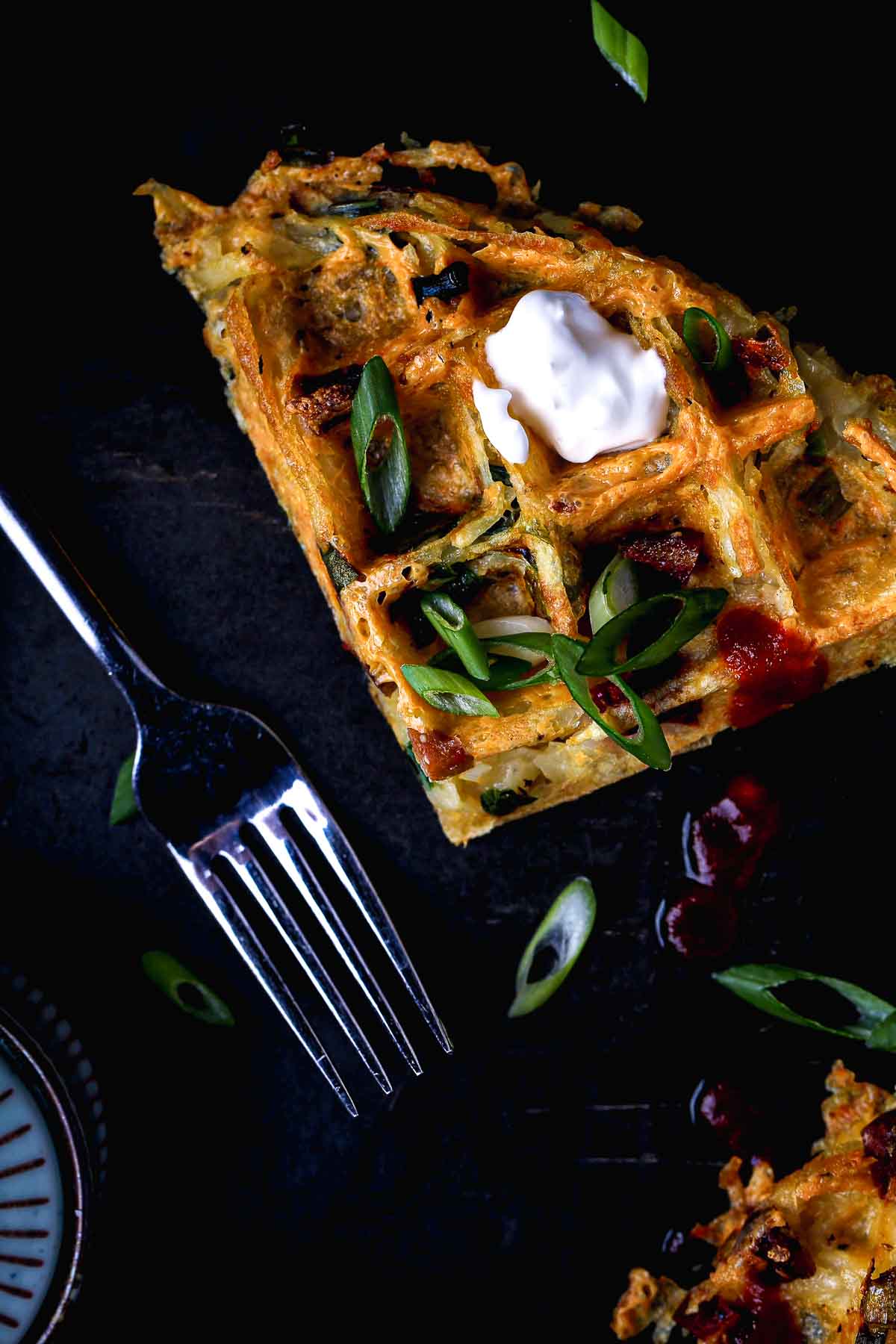 Close-up of crispy waffle edges and golden potato texture with scallions and vegan sour cream.