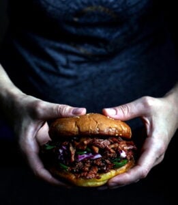 Two hands holding a vegan bbq pulled pork sandwich.