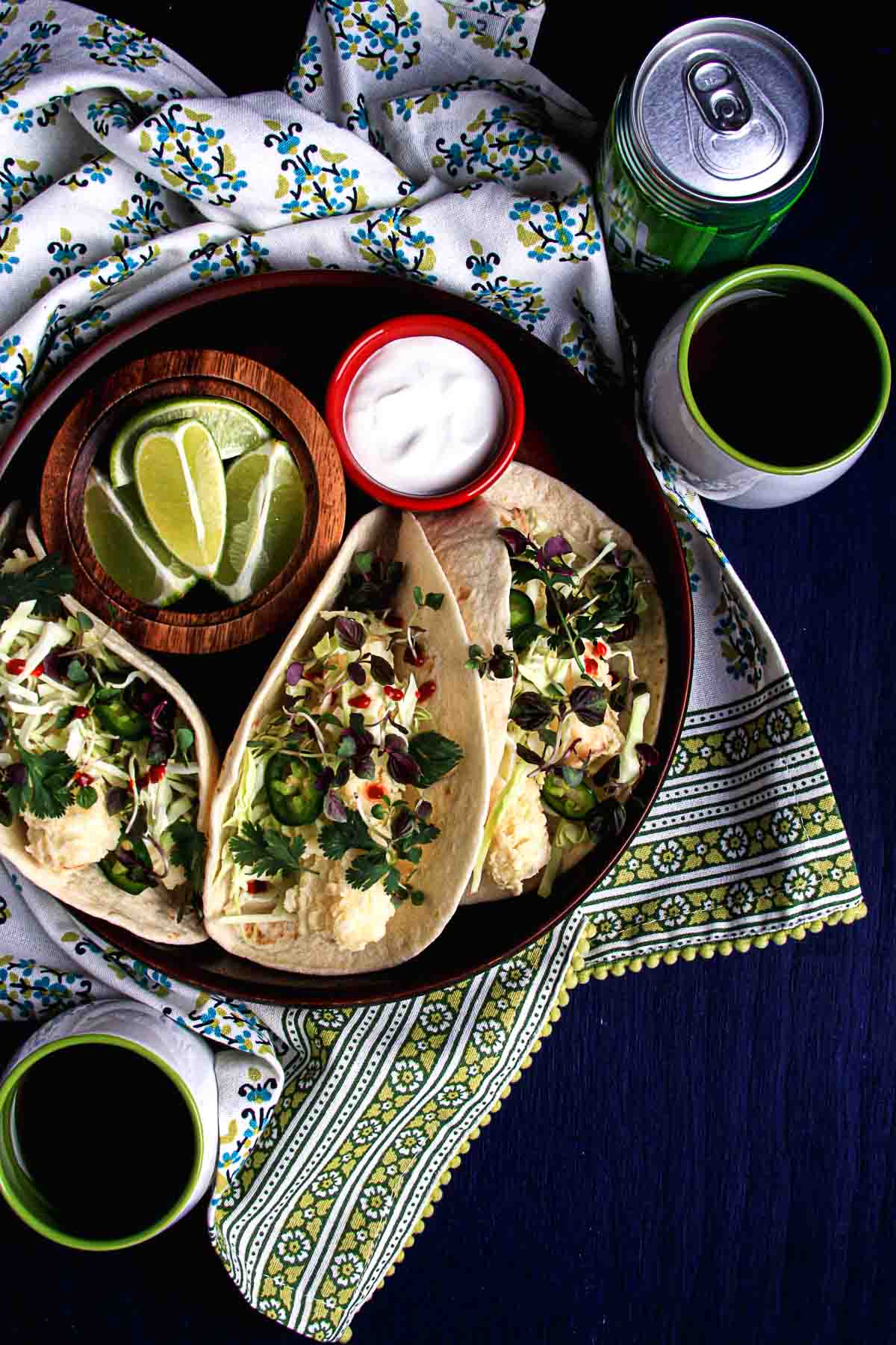Crispy hearts of palm tacos in a bowl with cabbage, jalapeño, cilantro, lime wedges, and vegan sour cream.