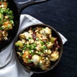 A small bowl of crispy kung pao Brussels sprouts with scallions and peanuts, styled next to a cast-iron skillet.