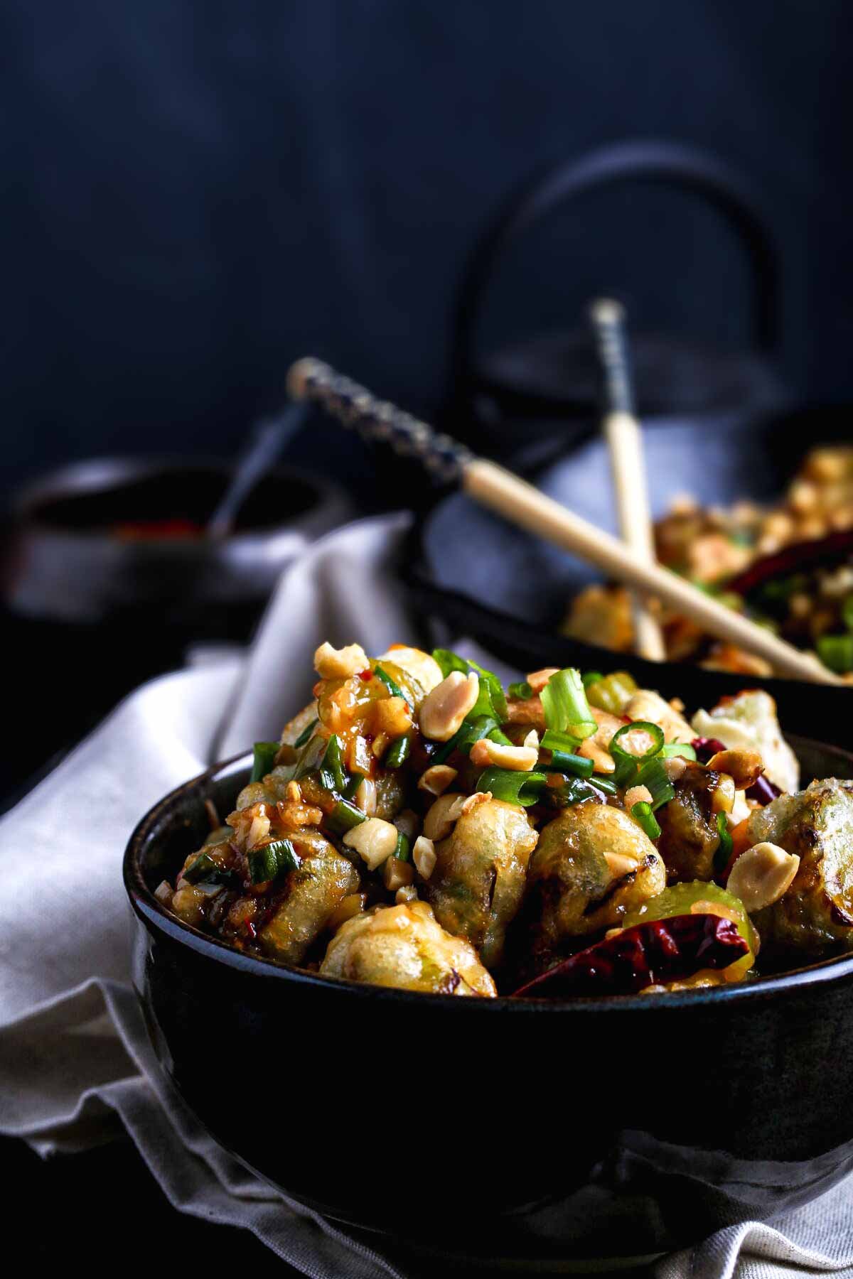 Crispy Kung Pao Brussels sprouts coated in a glossy sweet-spicy sauce, topped with peanuts and scallions.