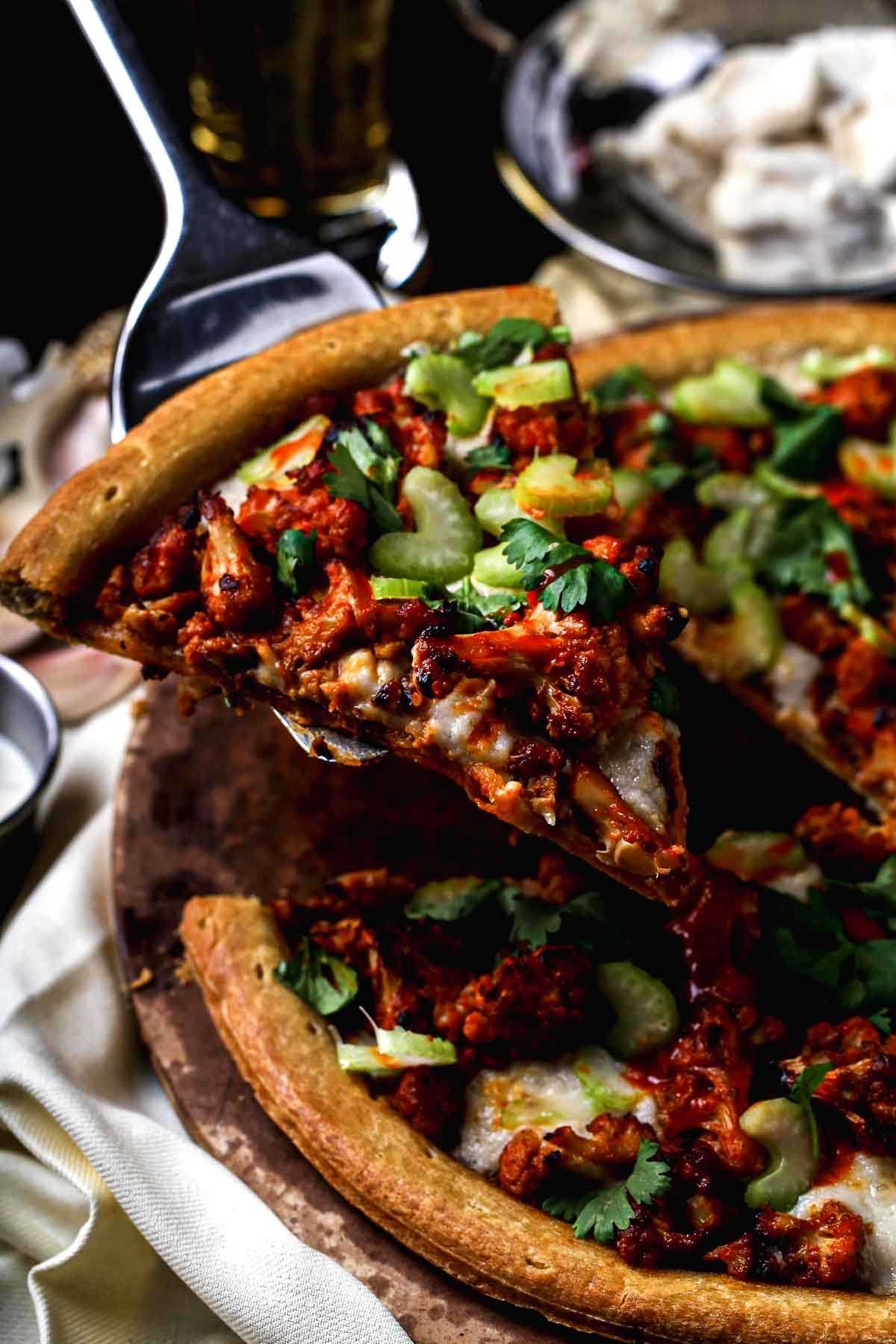 Close-up of a slice of buffalo cauliflower pizza with melted vegan cheese, roasted cauliflower, and fresh celery on a golden crust.