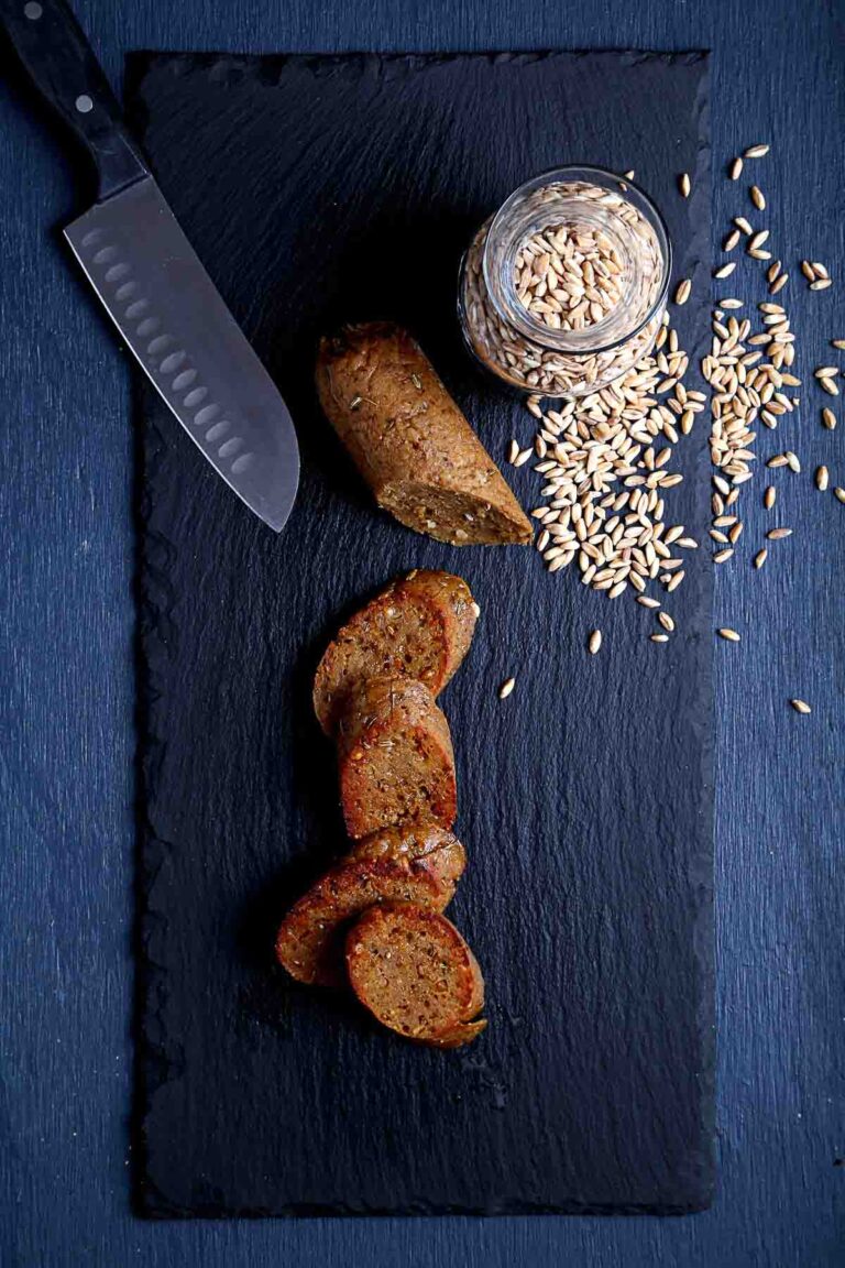 Sliced vegan Italian sausage browned in a skillet, showing the coarse farro texture inside.