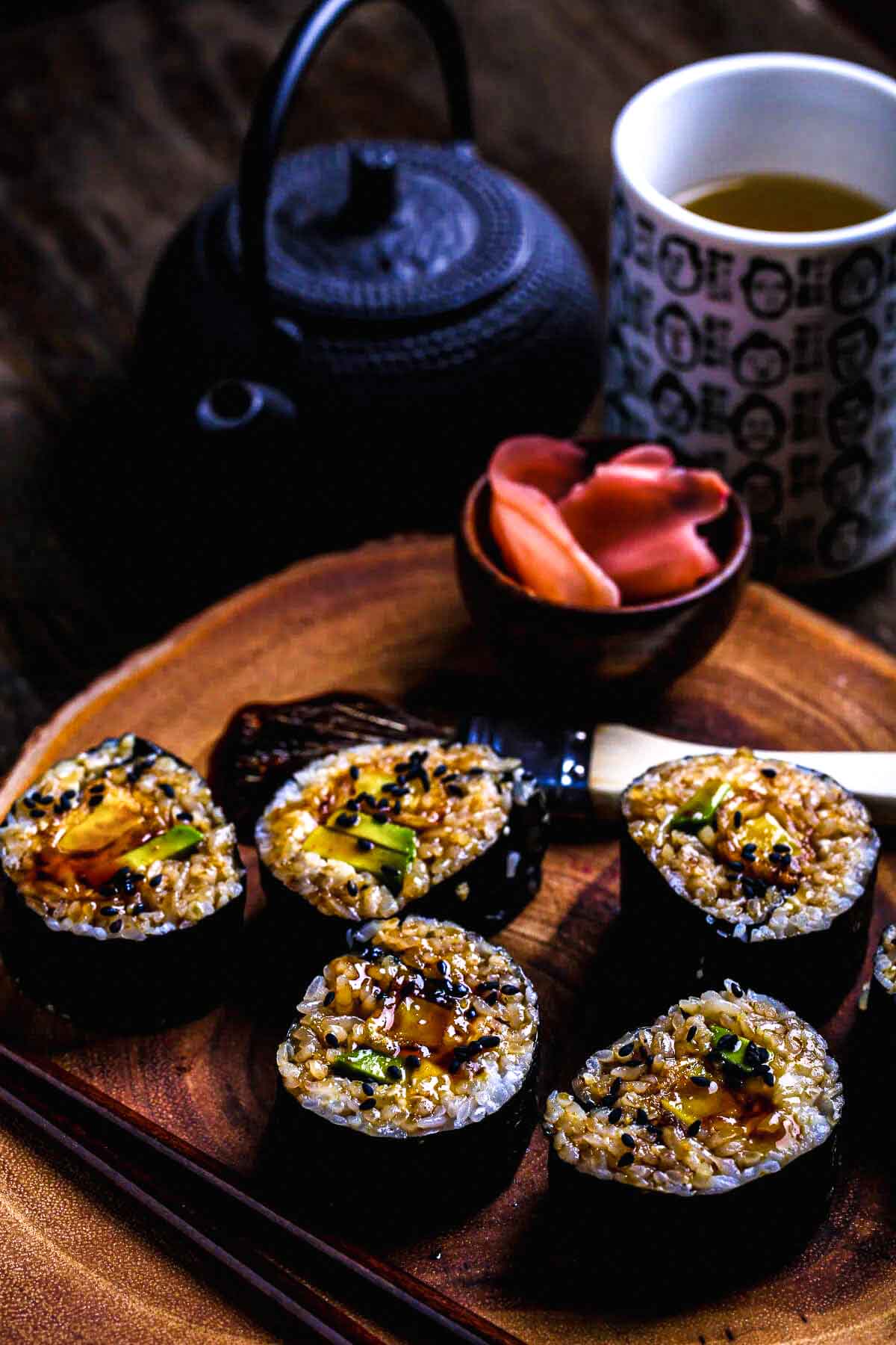 Close-up of vegan sushi rolls drizzled with glossy teriyaki glaze, sprinkled with sesame seeds, and paired with pickled ginger.