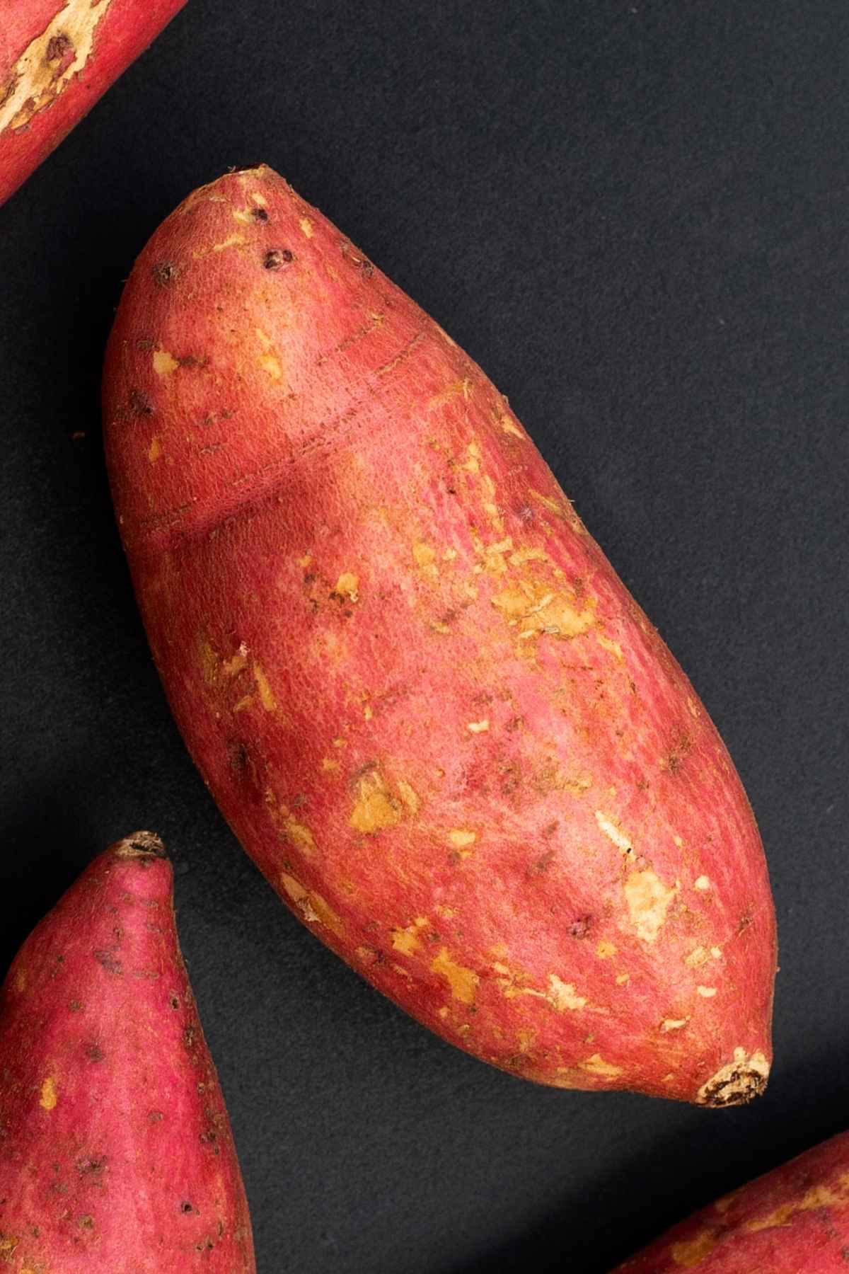 An unpeeled sweet potato against a dark background.