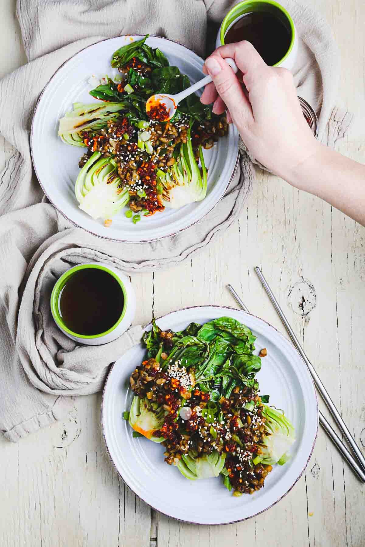 Hand spooning chili crisp over bok choy and oyster mushrooms.