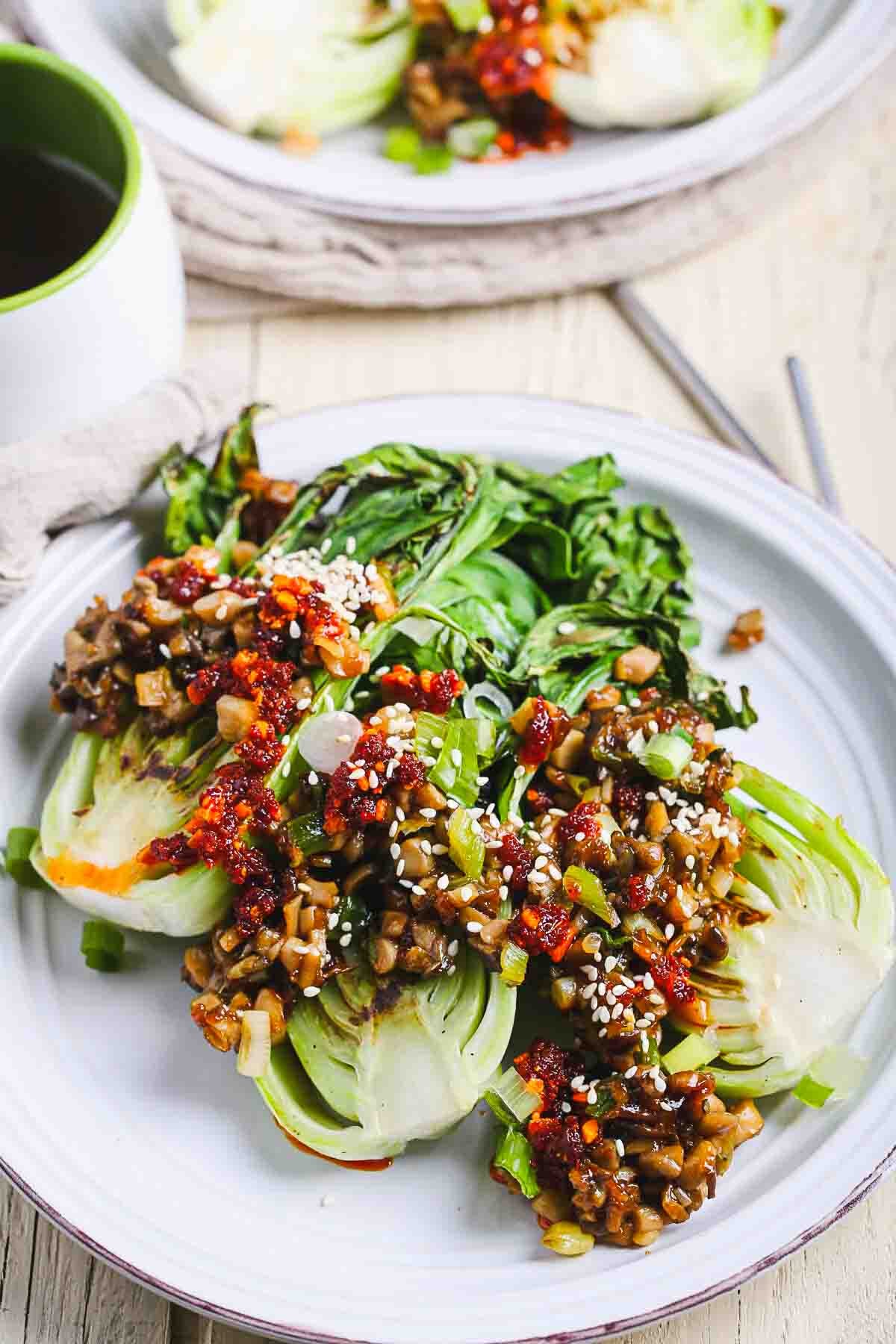 Bok choy and oyster mushrooms topped with chili crisp, scallions, and sesame seeds on a white plate.