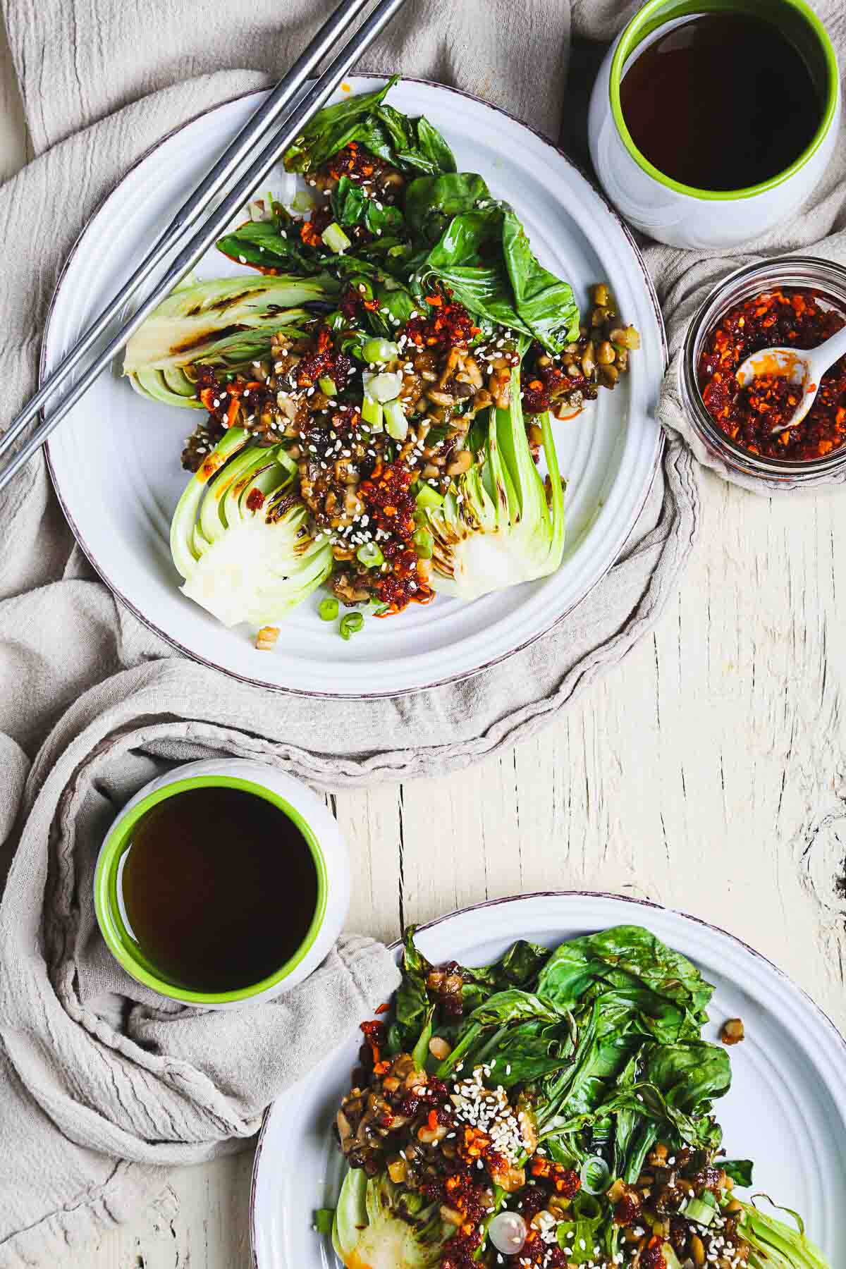 Two plates of bok choy with oyster mushrooms and chili crisp with chopsticks.