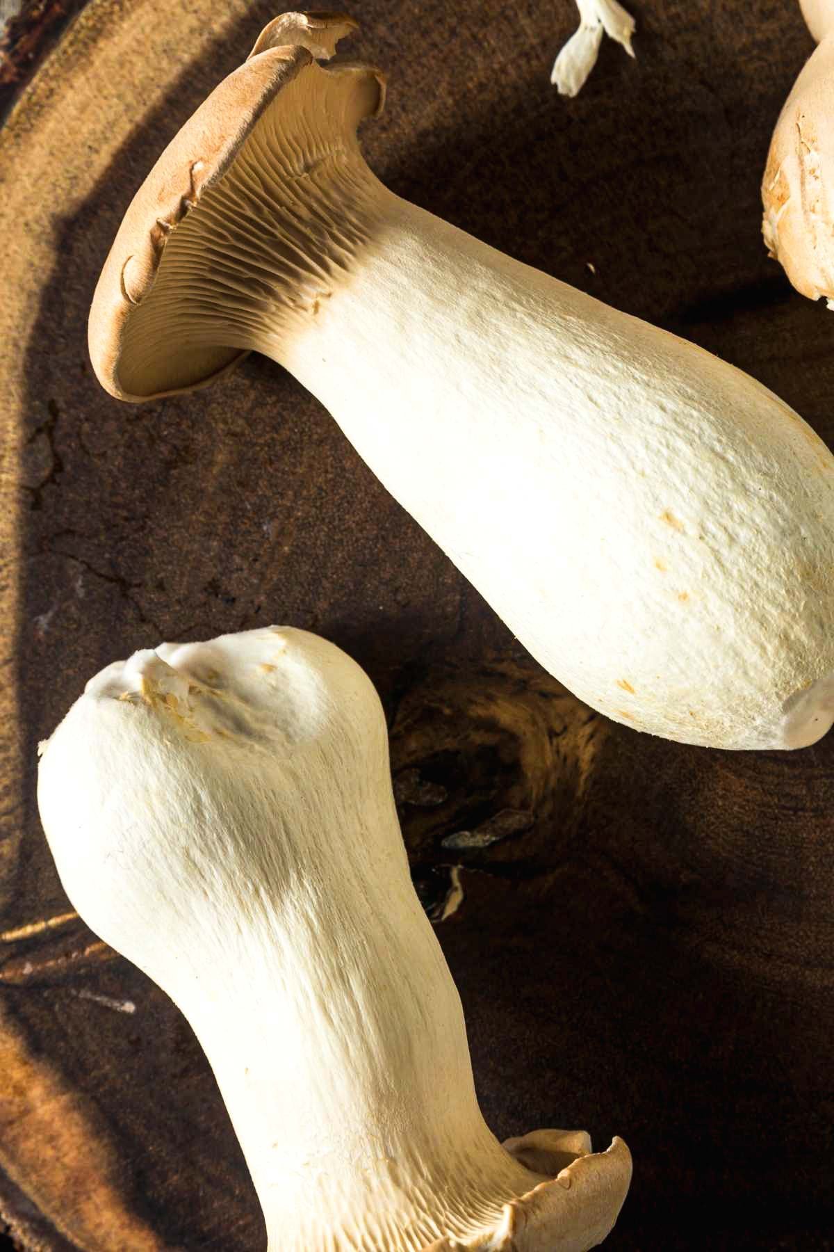 Fresh king oyster mushrooms on a wooden board, ready to be sliced into vegan scallops for creamy pasta.