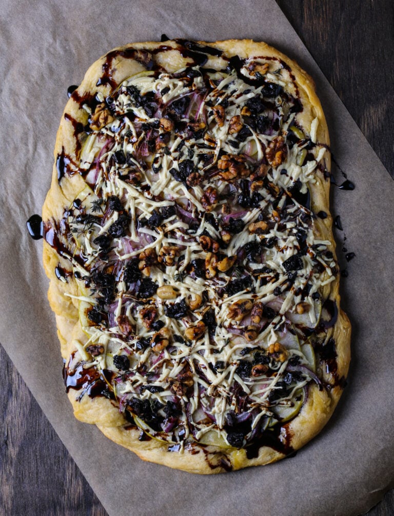 Focaccia pizza topped with green apple, oil-cured olives, toasted walnuts, vegan cheese, and balsamic glaze.
