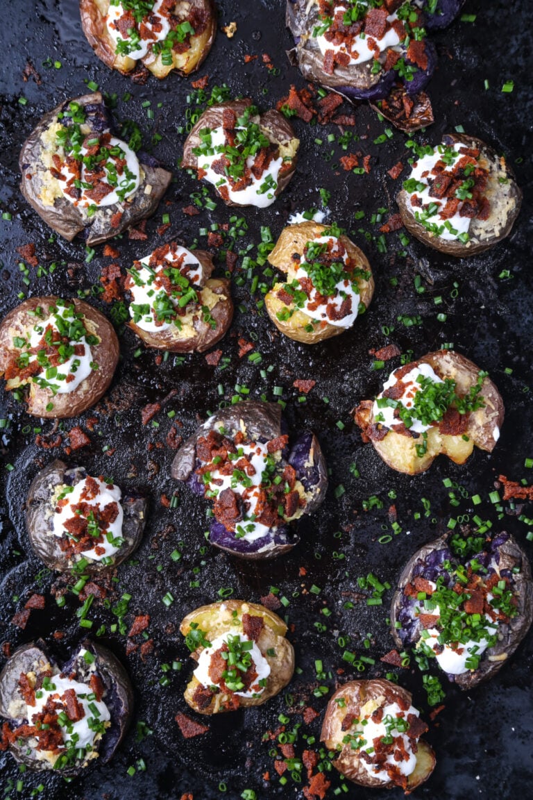 A top-down shot of loaded smashed potatoes on a baking sheet.