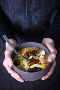 A bowl of hearty potato soup with tempeh cubes and vegan cheese.