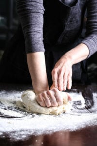 Hands kneading vegan pizza dough on a floured tabletop.