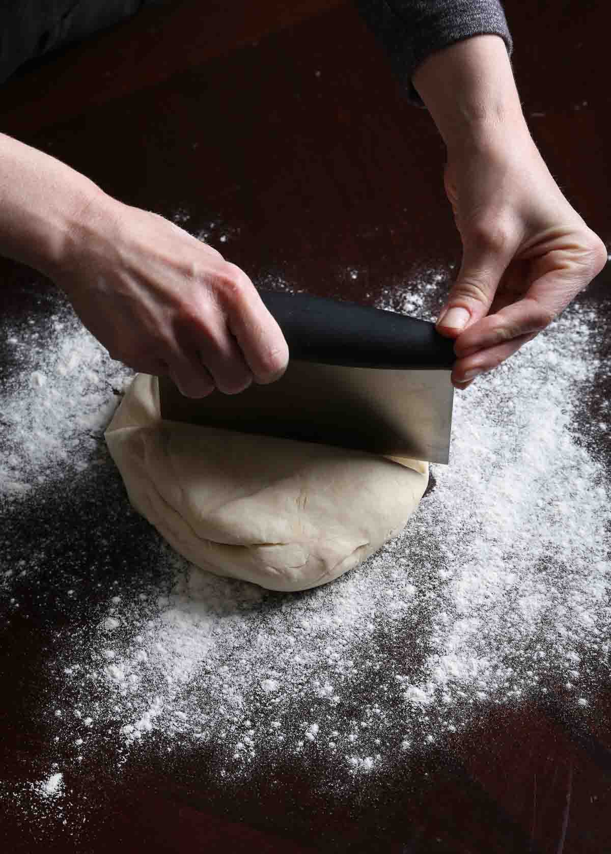 Pizza dough being divided into two even portions with a bench scraper.