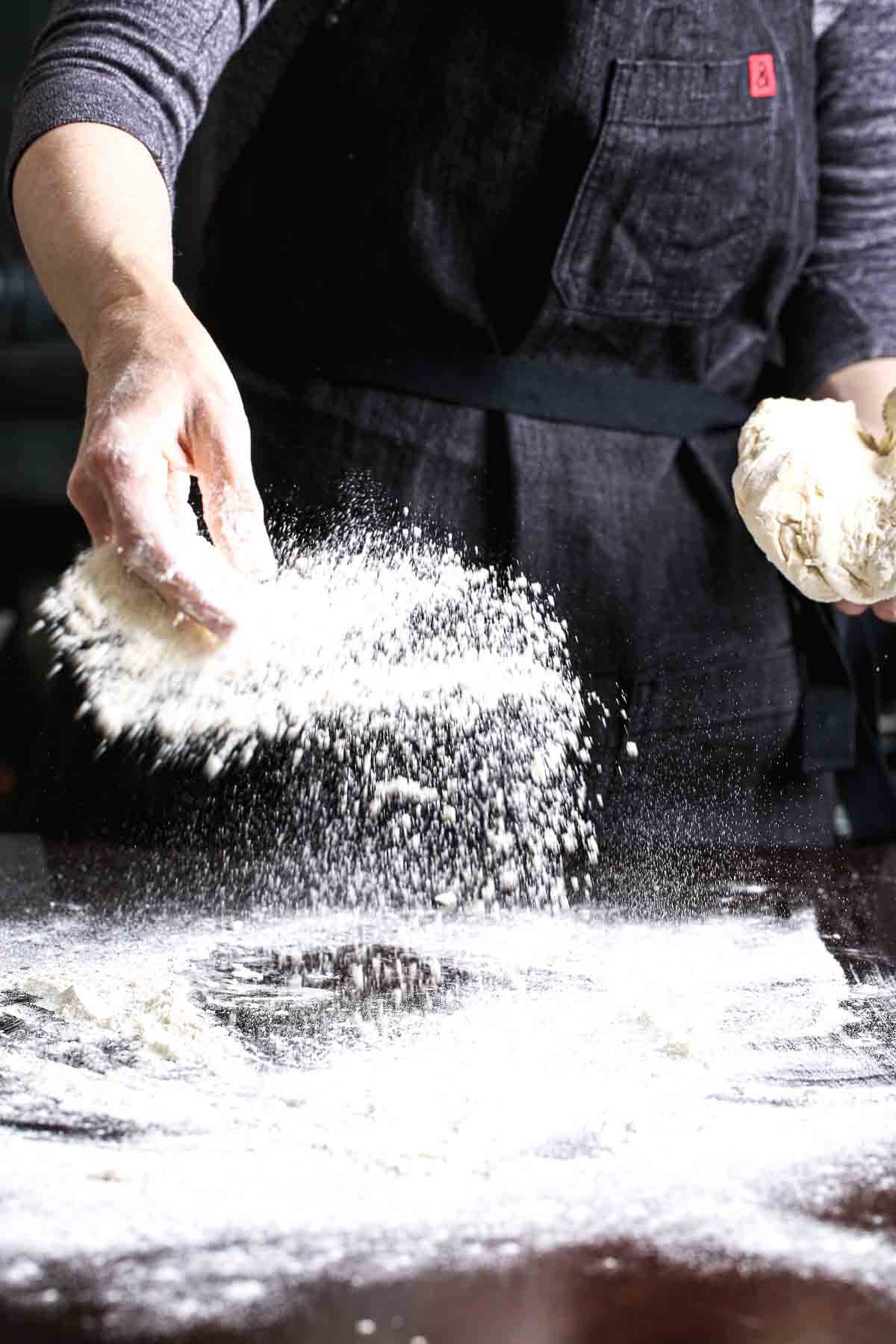 Flour being dusted across a countertop before kneading dough.