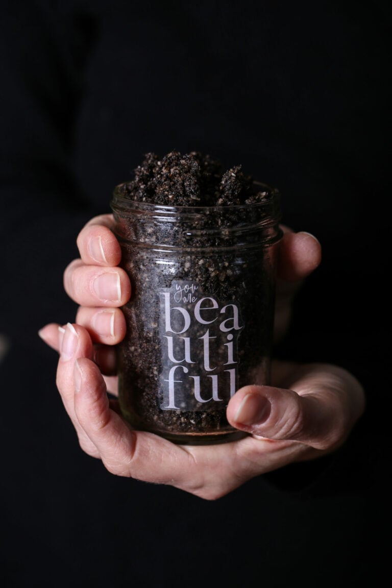 Two hands holding a glass mason jar of coffee sugar scrub.